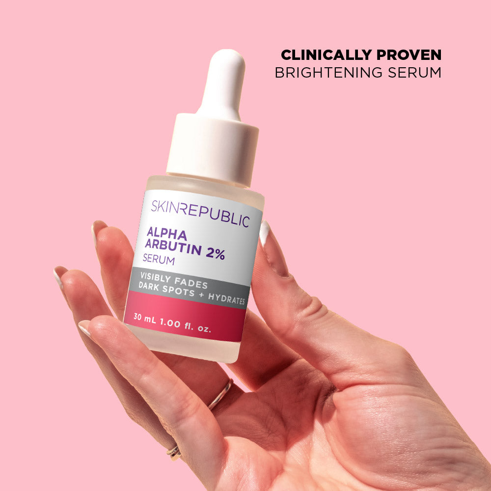 Hand holding a bottle of Skin Republic Alpha Arbutin 2% serum against a pink background
